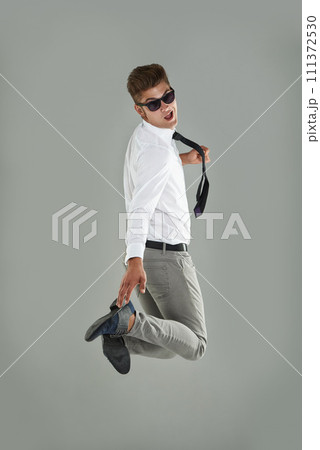 Businessman, jump and celebration for win in studio, professional and energy for success or victory. Male person, excited and sunglasses on gray background, playful and satisfaction for announcement 111372530