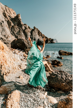 Woman green dress sea. Woman in a long mint dress posing on a beach with rocks on sunny day. Girl on the nature on blue sky background. 111373149