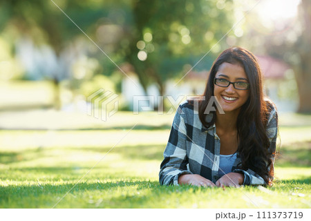 Portrait, park or happy woman on grass to relax for rest in garden, nature or field with peace. Travel, glasses and female person on break with smile for summer vacation, holiday or wellness on lawn 111373719