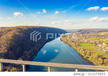 Aerial view of a road bridge over the river on an autumn sunny day. Village on the riverbank 111373855