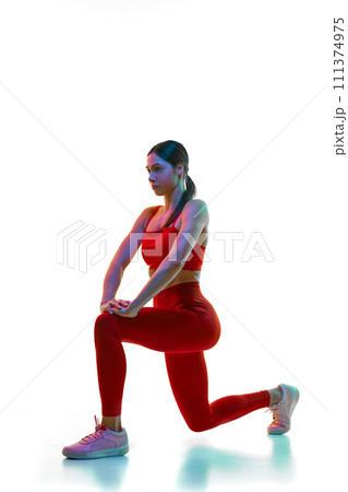 Young woman in red sportswear stretching and doing warming up exercises against white studio background in neon light Young woman in red sportswear stretching and doing warming up exercises against white studio background in neon light 111374975