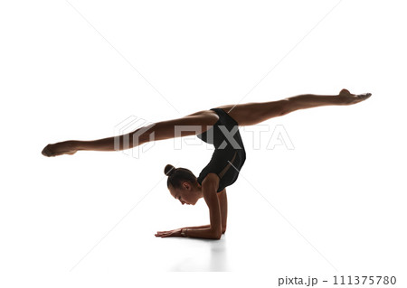 Tender teen girl, rhythmic gymnast in black suit performing, dancing against white studio background 111375780