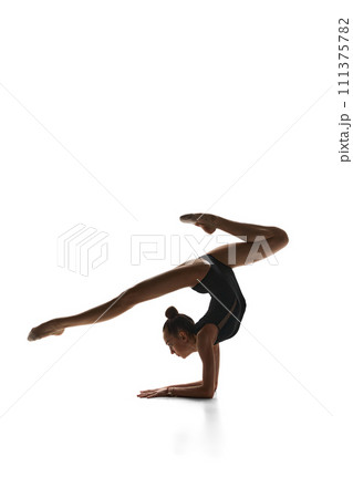 Tender teen girl, rhythmic gymnast in black suit performing, dancing against white studio background 111375782
