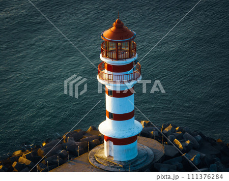 Red and white striped lighthouse on seaside in morning sunlight 111376284