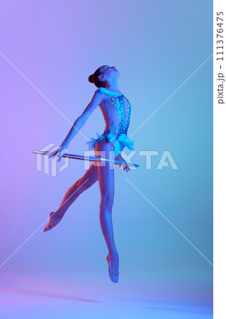 Full-length dynamic image of teen girl, rhythmic gymnast in motion, performing with hoop against gradient studio background in neon light 111376475