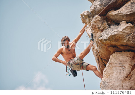 Mountain or rock climbing, cliff hanging and adrenaline junkie out on adventure and checking his safety equipment, hook and rope. Fearless man doing fitness, exercise and workout during extreme sport 111376483