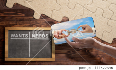 Two business hand holding pieces of a jigsaw puzzle with customer needs text on mobile phone screen with wants and needs table list on the chalkboard 111377346