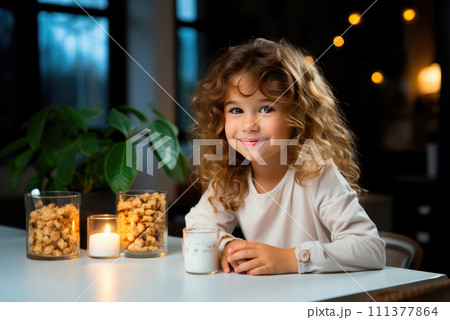 Child girl is sitting at the table and having dinner with yogurt with granola, grain cookies in the kitchen Child girl is sitting at the table and having dinner with yogurt with granola, grain cookies in the kitchen 111377864