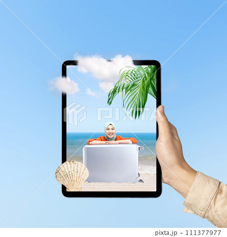 A human hand holding tablet with a screen view of an Asian girl in a scarf sitting with a suitcase on the beach with an ocean view and blue sky A human hand holding tablet with a screen view of an Asian girl in a scarf sitting with a suitcase on the beach with an ocean view and blue sky 111377977