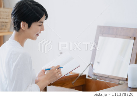 部屋で手帳に予定を書く女性 111378220