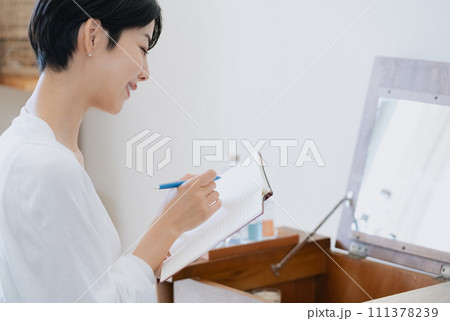部屋で手帳に予定を書く女性 部屋で手帳に予定を書く女性 111378239