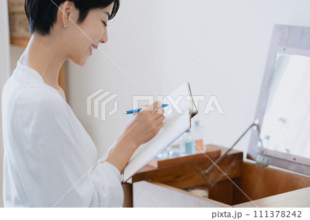 部屋で手帳に予定を書く女性 111378242