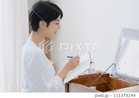部屋で手帳に予定を書く女性 111378249