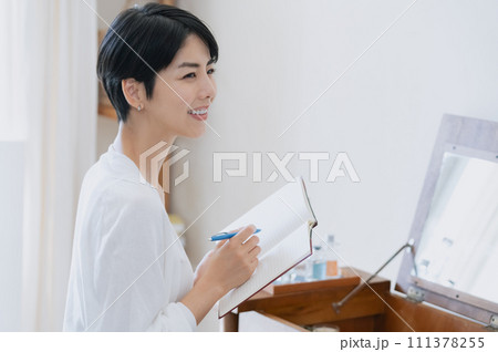 部屋で手帳に予定を書く女性 111378255