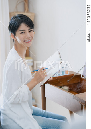 部屋で手帳に予定を書く女性 部屋で手帳に予定を書く女性 111378257