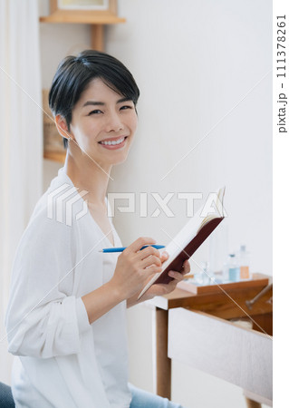 部屋で手帳に予定を書く女性 111378261