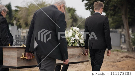 Coffin, men and pallbearers walking at graveyard ceremony outdoor at burial tomb. Death, grief and group casket at cemetery, carrying to funeral and family service of people mourning at windy event 111378882