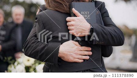 Funeral, graveyard and people hug for comfort, empathy and support at memorial service in cemetery. Depression, grief and sad man and woman for goodbye, mourning and burial for death with bible 111378890