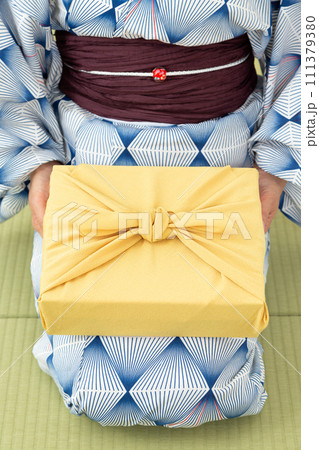 和室の畳に座ってお中元の風呂敷包みを持つ浴衣姿のミドル女性 111379380