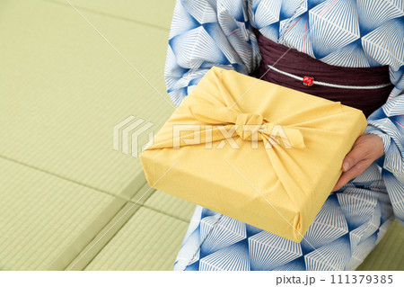 和室の畳に座ってお中元の風呂敷包みを持つ浴衣姿のミドル女性 111379385