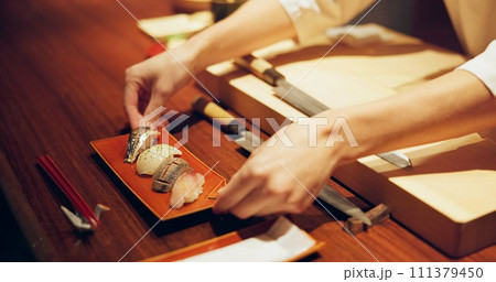Hands, cooking and chef serving sushi in restaurant for traditional Japanese cuisine or dish closeup. Kitchen, service or preparation of seafood and person working with gourmet recipe ingredients Hands, cooking and chef serving sushi in restaurant for traditional Japanese cuisine or dish closeup. Kitchen, service or preparation of seafood and person working with gourmet recipe ingredients 111379450