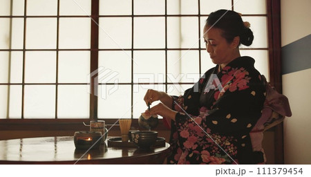 Tea, Japanese woman and traditional with a teapot, flavor and drinking ritual with herbal beverage and leaves. Asian person with culture and ceremony with Kimono, home and calming with wellness 111379454