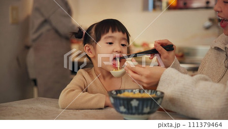 Family, Japanese and woman feeding daughter in kitchen of home for growth, health or nutrition. Food, girl eating ramen noodles in apartment with mother and parent for diet or child development 111379464