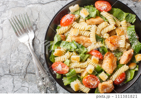 Caesar salad with grilled chicken, pasta, romaine lettuce, parmesan, tomatoes and croutons close-up in a bowl. Horizontal top view 111381821