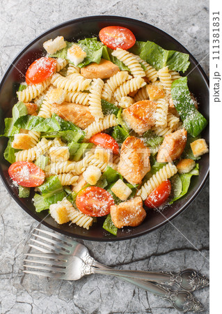 Caesar salad fusilli pasta with chicken, romaine lettuce, parmesan, tomatoes and croutons close-up in a bowl. Vertical top view 111381831