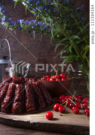 Delicious chocolate cake with sweet cherry, vintage kettle and bouquet of blue flowers on dark wooden background.. Delicious chocolate cake with sweet cherry, vintage kettle and bouquet of blue flowers on dark wooden background.. 111384164