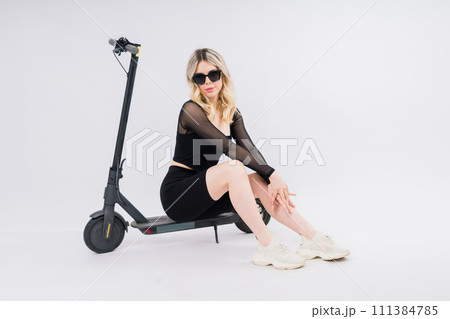 A blonde woman on red background sitting on electro scooter and resting, copy space 111384785
