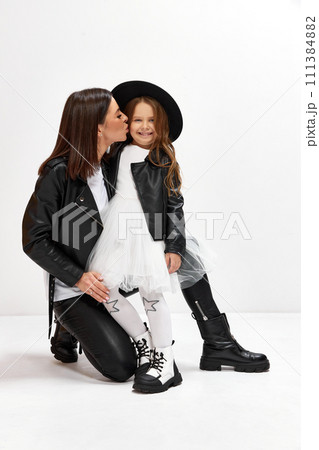 Happy young brunette woman, other cissing her little kid, daughter against white studio background. Same style clothes Happy young brunette woman, other cissing her little kid, daughter against white studio background. Same style clothes 111384882