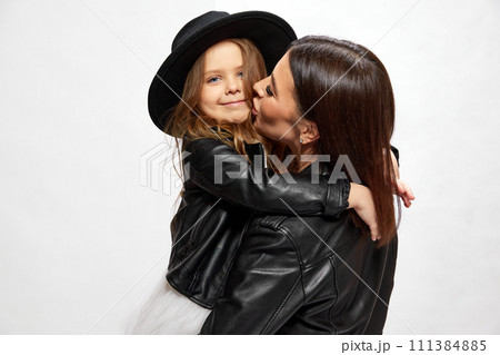 Happy young brunette woman, other cissing her little kid, daughter against white studio background. Same style clothes 111384885