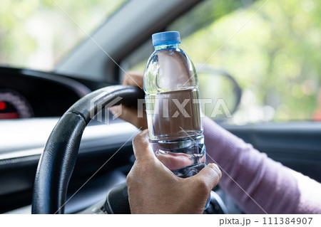 Asian woman driver holding bottle for drink water while driving a car. Plastic hot water bottle cause fire. 111384907
