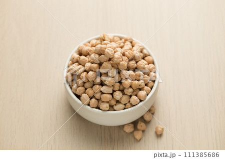 Chickpeas in a small white bowl on a wooden table. 111385686