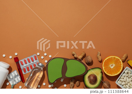 Paper liver, medical supplies, nuts, avocado and orange on brown background, space for text 111388644