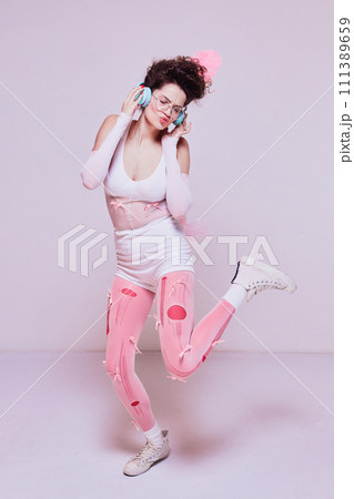 Stylish young woman listening to music in headphones and emotionally singing against pastel pink background. Online electronics store banner 111389659