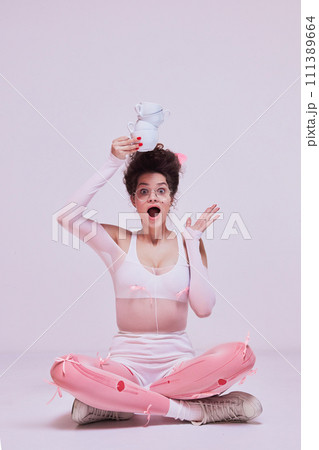 Promotion for a playful and creative cooking class. Surprised woman balancing teacups, playful gesture, pink outfit, fun concept. Promotion for a playful and creative cooking class. Surprised woman balancing teacups, playful gesture, pink outfit, fun concept. 111389664