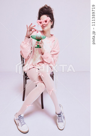 Young pretty woman sitting o chair in pink comfortable clothes and sunglasses, eating cake. Coziness at home. Life balance. Sweet tooth Young pretty woman sitting o chair in pink comfortable clothes and sunglasses, eating cake. Coziness at home. Life balance. Sweet tooth 111389719