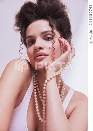 Portrait of beautiful young woman with nude, tender makeup look, wearing pear necklace, posing against pastel background. Self-care and femininity. Portrait of beautiful young woman with nude, tender makeup look, wearing pear necklace, posing against pastel background. Self-care and femininity. 111389745