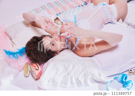 Top view image of tender young woman in elegant vintage lingerie lying on bed. Luxury bedding ad focusing on elegance and dreamy aesthetics. 111389757