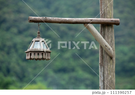 Thai traditionan wooden lantern hang on wooden post with green blurred background. 111390257