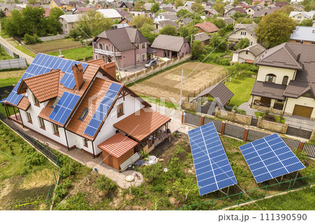 Aerial top view of new modern residential house cottage with blue shiny solar photo voltaic panels system on roof. Renewable ecological green energy production concept. Aerial top view of new modern residential house cottage with blue shiny solar photo voltaic panels system on roof. Renewable ecological green energy production concept. 111390590