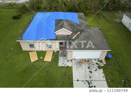 Top view of leaking house roof covered with protective tarp sheets against rain water leaks until replacement of asphalt shingles. Damage of building rooftop as aftermath of hurricane Ian in Florida 111390749