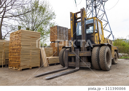 Large lift truck and stacks of new wooden boards and studs at the lumber yard. Wooden plates on piles for furniture materials Large lift truck and stacks of new wooden boards and studs at the lumber yard. Wooden plates on piles for furniture materials 111390866