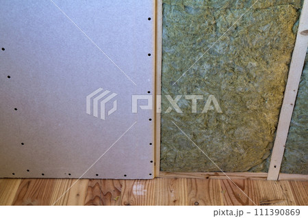 Wooden frame for future walls with drywall plates insulated with rock wool and fiberglass insulation staff for cold barrier. Comfortable warm home, economy, construction and renovation concept. Wooden frame for future walls with drywall plates insulated with rock wool and fiberglass insulation staff for cold barrier. Comfortable warm home, economy, construction and renovation concept. 111390869