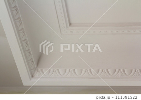 Ornamental white molding decor on ceiling of white room close-up detail. Interior renovation and construction concept. Ornamental white molding decor on ceiling of white room close-up detail. Interior renovation and construction concept. 111391522