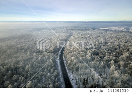 Aerial view of winter landscape with snow covered woods and black asphalt forest road on cold wintry day 111391550