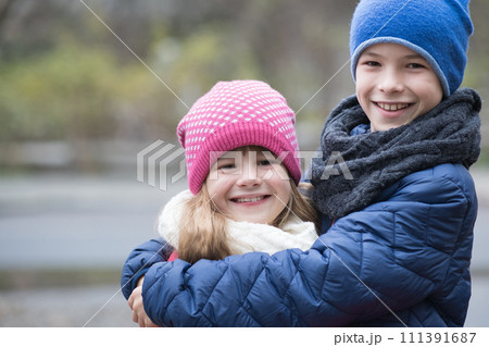 Two children boy and girl hugging each other outdoors wearing warm clothes in cold autumn or winter weather. Two children boy and girl hugging each other outdoors wearing warm clothes in cold autumn or winter weather. 111391687