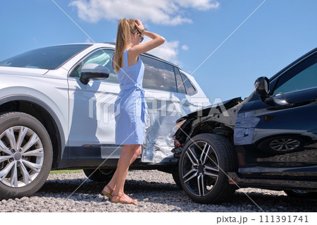 Sad female driver standing on street side shocked after car accident. Road safety and vehicle insurance concept 111391741